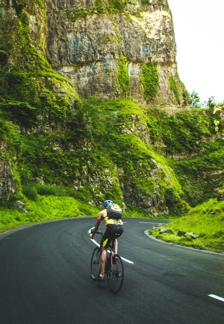 Ciclista pedalando em estrada montanhosa, mostrando ciclismo de estrada. Foto para web design de site de esportes.
