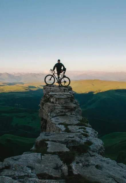 Homem com bicicleta de montanha no topo de uma rocha, em um ambiente natural. Web design de portfólio de esportes outdoor.